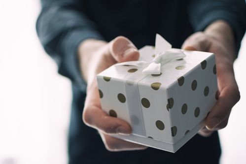 person holding white gift box with gold polka dots and white ribbon