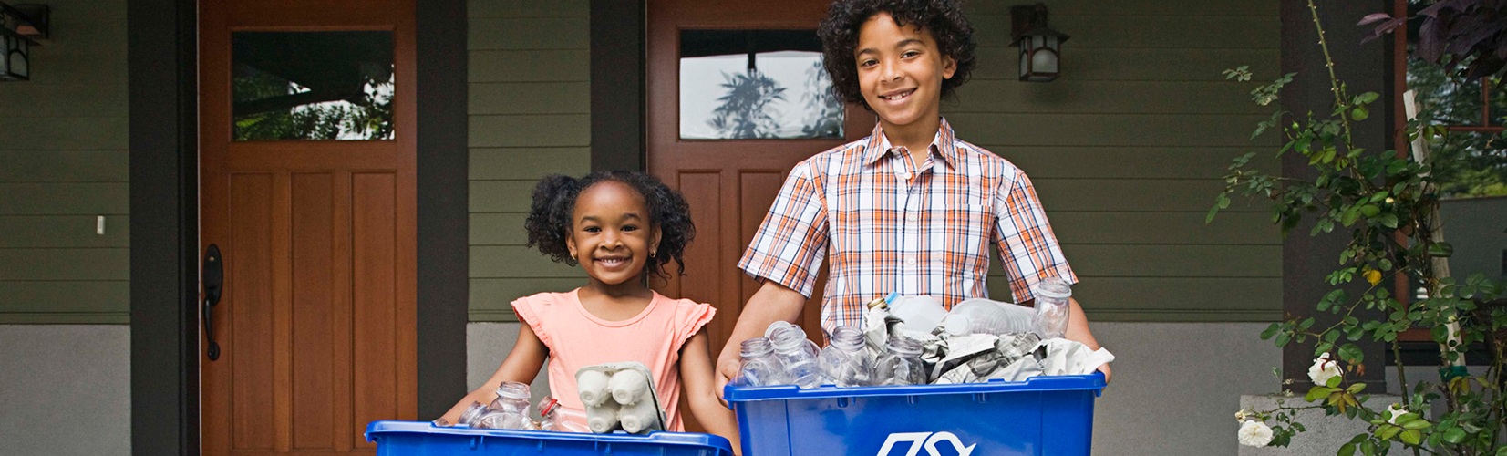Two cheerful children standing outside their home, proudly holding bins filled with recyclable materials, promoting sustainability.
