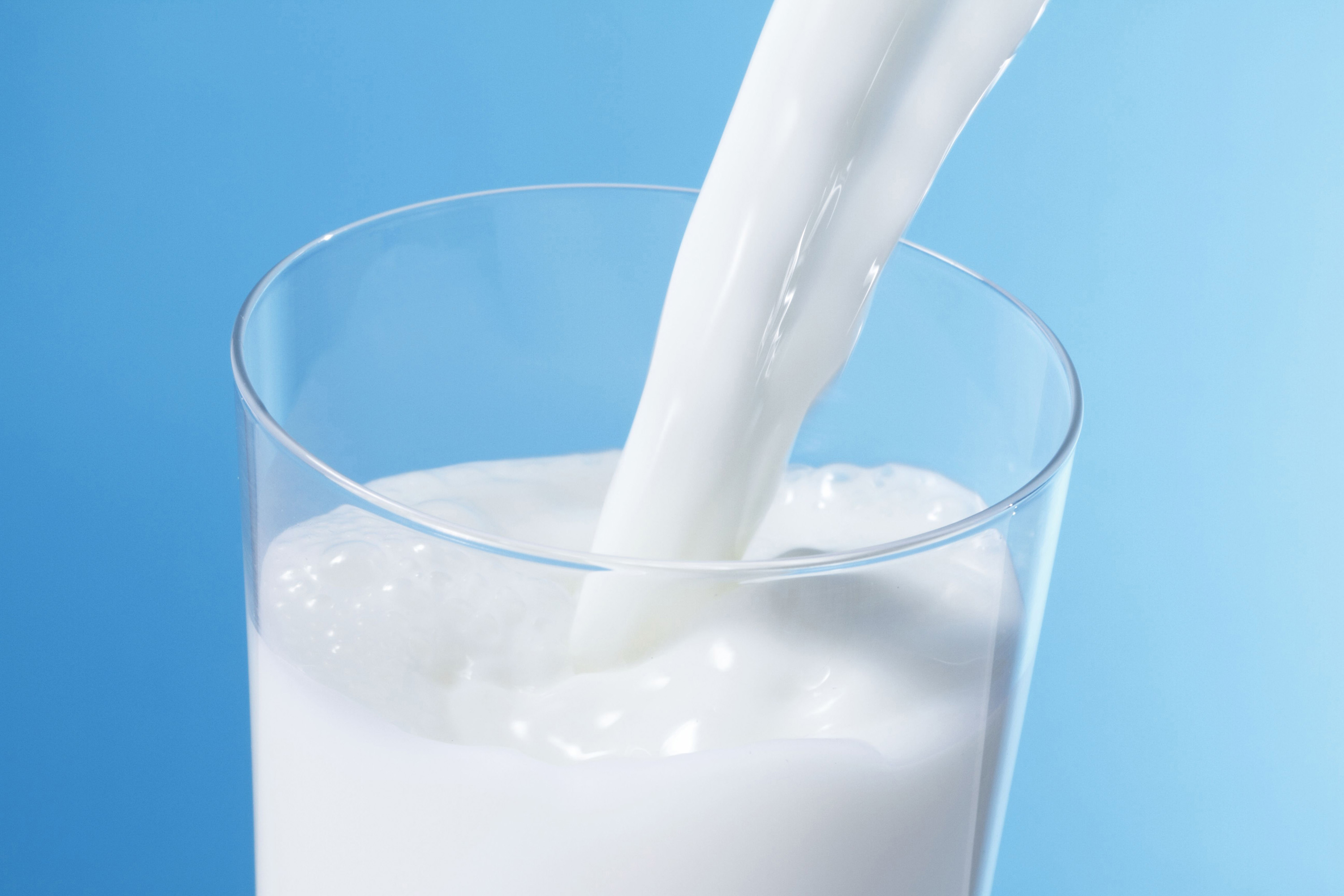 Pouring milk in glass with blue background