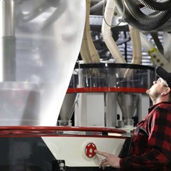 A person is operating a blown film extrusion machine inside a warehouse.