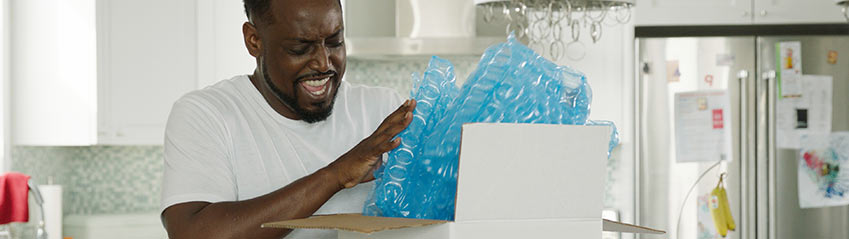 A person is happily opening a white cardboard box package with HC Inspyre blue protective packaging.